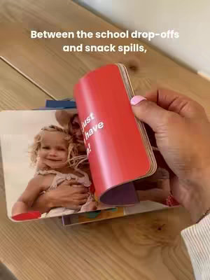 A person's hand holds open a multi-page photo journal, revealing images of a child and an adult. Text overlay is displayed at the top and on the book covers.