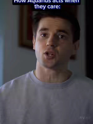 A man with short dark hair features in the frame. The lighting seems natural, and he is dressed in a simple gray sweatshirt. Behind him, there are glimpses of a room with what appears to be a framed picture hanging on the wall. Text overlayed on the image reads the phrase 'How Aquarius acts when they care:'.