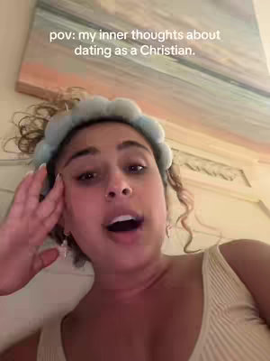 A selfie-style shot features a young woman, looking up and slightly to her left, with her mouth open as if speaking. She has curly light brown hair pulled back with a light sky blue headband. The background is a blurred room, with the top portion showing a painting in muted colors.