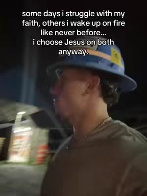 A man in a hard hat and casual clothing is filmed from the side, walking at night. The background is blurred, suggesting a dimly lit or nighttime setting. Text overlays the image.