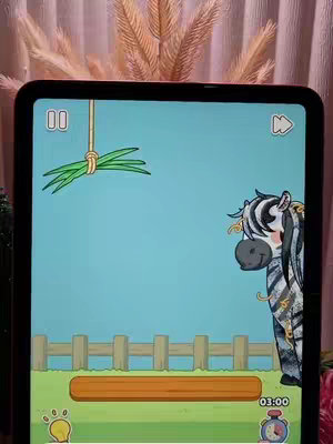 The image shows a game on a tablet. The game displays a cartoon zebra with a happy face on the right side, looking at a bundle of grass hanging from above. The background is light blue with details like a wooden fence and a timer at the bottom.