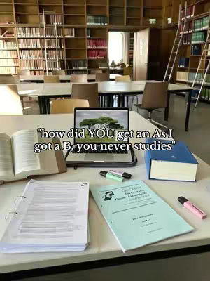 A well-lit library setting with books shelves on both sides. On the foreground, a white desk with a laptop, open book, a notebook, and papers. The overlayed text asks about getting an A, while the poster got a B and the user always studies.