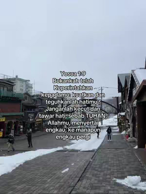 The image shows a snowy street scene. Buildings with dark roofs line the sides, with a pale sky above. In the center, a text overlay provides a Bible verse.