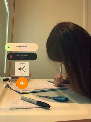A desk with stationary and a person out of view writing with a pen. The overlay shows phone settings icons.
