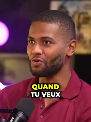 A medium shot of a Black man speaking into a microphone; a title overlay with yellow text appears below the man, and a blurred, vibrant magenta light is visible in the background outside the frame.