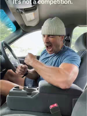 A man is shown inside a vehicle, looking distressed with his mouth open, wearing a beanie. The image is framed from the chest up, showcasing the man's upper body and the car's interior.