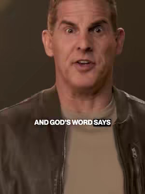 A medium shot features a middle-aged man with short, light brown hair and an open mouth, as if he is speaking. He is wearing a brown jacket over a light-colored shirt. The background is a blurred, neutral tone, and white text reading 'AND GOD'S WORD SAYS' overlays the shot.