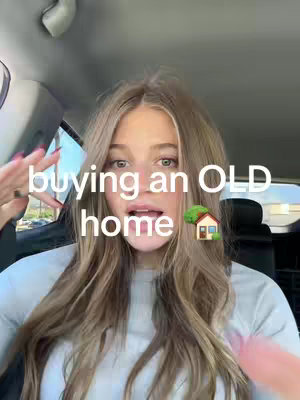 A young woman with long blonde hair is seated in a car, talking to the camera. The overlay text reads "buying an OLD home" accompanied by a house emoji. The background appears to be a car interior.