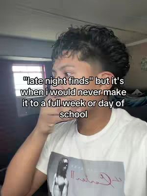 A young man, likely in his late teens or early twenties, is captured in a selfie-style video. He has short, neatly styled dark hair.  He's wearing a white t-shirt that features a graphic print. The background shows a hint of a room.