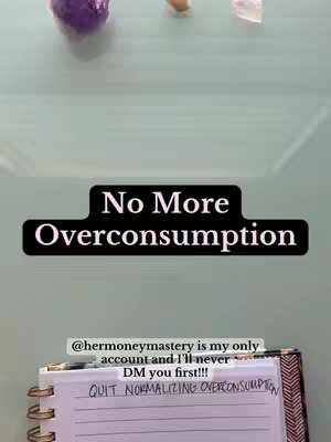 A top-down shot showing a light-colored surface, possibly a desk or table. There are several objects visible, including a purple crystal, a small beige object, and a clear crystal. A notepad with a handwritten message that says 'QUIT NORMALIZING OVERCONSUMPTION' is also visible. A black banner with the words 'No More Overconsumption' and other related text are placed above the notebook.