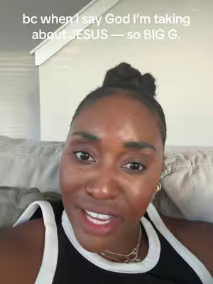 A selfie-style shot featuring a woman with dark hair styled in a bun. She wears a black and white tank top. Her features are illuminated, highlighting her expression and the background is a neutral white. Text at the top reads, "bc when I say God I'm talking about JESUS — so BIG G."