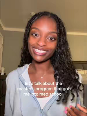 A young woman with long, braided hair is smiling directly at the camera, wearing a light blue zip-up hoodie and a necklace. The background is a blurred interior setting, featuring neutral-colored walls and a glimpse of a bed. Text overlayed on the image reads, 'let's talk about the master's program that got me into med school'.