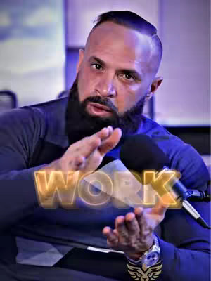 A man with a trimmed beard and shaved head is the focal point, gesturing with his hands as if explaining something. The image is framed from the chest up, set against a blurred background with a microphone visible and the word 'WORK' overlaid in a glowing, stylized font.