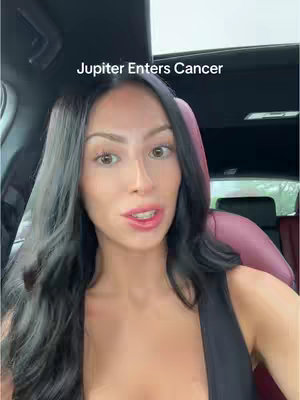 A medium shot shows a woman inside a car, looking directly at the camera and speaking. The foreground is dominated by the woman's face and upper body, while the background includes the car's interior, with a hint of scenery visible through the windows.. Text overlayed at the top reads 'Jupiter Enters Cancer.'