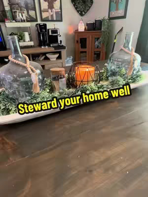 A wooden table is in the foreground, with a floral arrangement as a centerpiece in the background. The arrangement looks to be indoors, is on a wooden table.