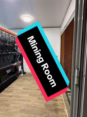The cover image shows a diagonal shot of a mining room, showcasing the interior of the facility. The focus is on a vibrant text overlay that reads "Mining Room," placed at an angle against a backdrop of the room's contents. The room itself is filled with rows of servers and supporting computer equipment, indicating its use for cryptocurrency mining operations. The lighting is diffused, highlighting the equipment setup and the overall functionality. A door frame is visible in the lower right. The floor is wooden.