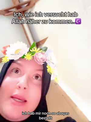 A woman with light skin and dark hair framing her face is the primary subject. She wears a black hijab. Adorning her head is a floral crown featuring white petals and hints of yellow and pink. The woman is positioned in front of a bright backdrop. She is speaking. In the foreground, text is superimposed over the image.