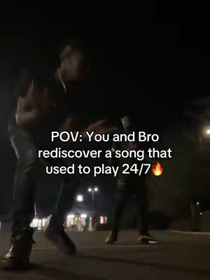 Two men are walking at night, likely in a parking lot or street, with one in the foreground and another slightly behind, partially obscured. The scene is dark, with the street lights illuminating the area. Text overlayed on the image says 'POV: You and Bro rediscover a song that used to play 24/7'