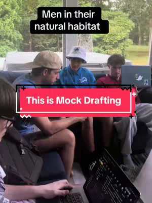 A group of young men are gathered, presumably on a bus or similar vehicle, with trees visible through the window. They are interacting over laptops. The text overlay 'Men in their natural habitat' and 'This is Mock Drafting' are displayed.