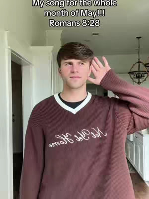 A young man in a brown sweater with a white trim stands in a well-lit room. He is listening into his right ear with his right hand. The upper left corner of the image is a text overlay.
