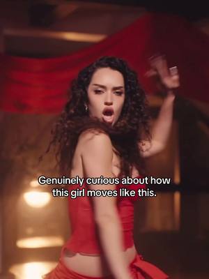 A woman wearing a red outfit strikes a dynamic pose, with one arm raised. A text overlay appears in white.  A red curtain creates the background.