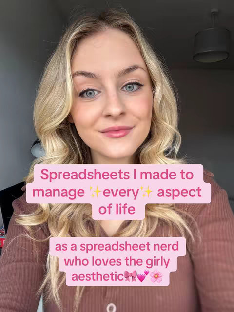 A selfie-style shot with a blonde woman centered, smiling directly at the camera. She has light eyes and is wearing makeup. A pink rectangular text overlay covers a portion of her face, reading, "Spreadsheets I made to manage ✨ every ✨ aspect of life". Below this, another pink text overlay states, "as a spreadsheet nerd who loves the girly aesthetic 💕🎀🌸". The background is softened, and the lighting is natural.