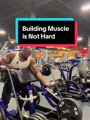 A muscular man in a white tank top is working out with a cable machine in a gym. Above him is a rectangular text box with the words 'Building Muscle is Not Hard.'