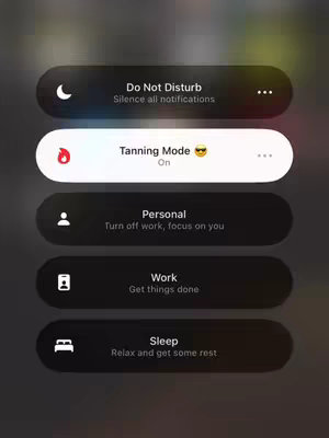 The image shows a white notification with the text "Tanning Mode On", a sunglasses emoji followed by other notifications which are mostly black with white text in a dark setting.