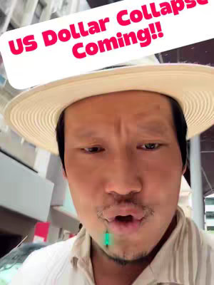 The cover image shows a man looking directly at the camera in front of a city's building. Text reading "US Dollar Collapse Coming!!" is shown in a white box with a maroon outline. The man is wearing a beige hat.