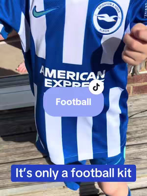 The cover image shows a young child wearing a blue and white Brighton & Hove Albion football kit. The jersey has the team logo on the chest and sponsor logos. Two text overlays are placed on the image, one reading 'Football' in a rounded rectangle and the other 'It's only a football kit' at the bottom in a rectangle shape.