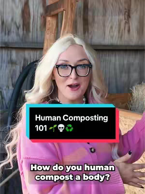 A woman with blonde hair and black-framed glasses is centered in the frame, smiling slightly with an open mouth. She wears a pink cardigan over a pink top. Behind her, there's a wooden structure and a glimpse of a hay bale. The overlay text includes the title 'Human Composting 101' in a box, along with the question 'How do you human compost a body?'