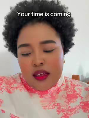 A close-up shot of a woman’s face. She has dark, curly hair, and her skin has a highlighted warmth in the cheeks and lips. The text overlay reads "Your time is coming". The background is a light, undefined color.