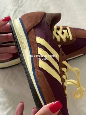 The cover image shows a close-up of a pair of Adidas sneakers. The sneakers are a mix of brown, burgundy, and yellow colors. The Adidas three stripes logo in yellow is visible on the side. The tips of a hand with red nail polish is partly visible on the background. Text overlay says, 'the perfect fall trainers for 2025'.