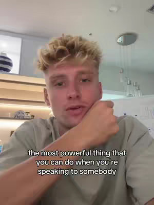 A young, fair-skinned man with short, blonde hair is the central figure in a selfie-style video. He's positioned in a well-lit interior, leaning his head on his hand and looking directly at the camera with a slight expression of intrigue. Below him, a text overlay in a sans-serif font provides context for the video.