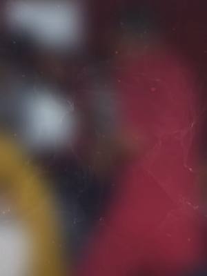 An out-of-focus abstract image with swirling colors of burgundy, yellow, and white. The composition is blurred, with the colors blending together. There are several vague light spots and faint streaks across the image.