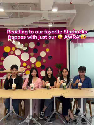 A group of young adults are seated at a table, each holding a Starbucks Frappuccino. The background is a brightly colored wall with circular and abstract decorations. Text overlays at the top of the image.