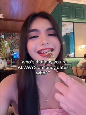 A selfie-style image of a young person, likely female, smiling and holding a fork with food in their mouth, against a blurred restaurant background. The person has long, dark hair, bright red lipstick, and braces. Text is overlaid on the image.