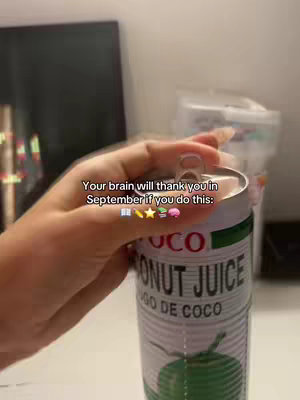 A close-up shot of a hand holding a can of coconut juice, with text overlayed. The background is blurred and shows a computer screen and another container.
