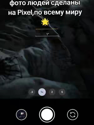 A smartphone camera interface overlaying a blurred image of a surface, possibly a bed or a textured material. The interface includes a central white circle (shutter button), a button on the left with a small image, likely for settings or gallery, and a button on the right to switch cameras. The zoom options are at the bottom, marked with numbers. At the top, it has white text on a dark background.
