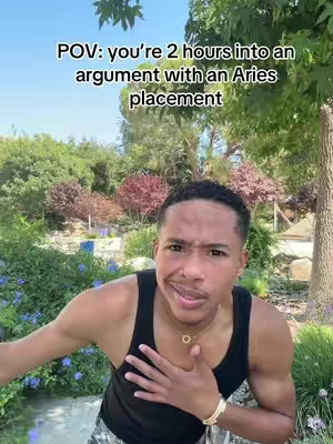 A man with a slightly perplexed expression stands outdoors, with green foliage and trees in the background. Text overlays the image, and he is wearing a black tank top and a gold necklace.