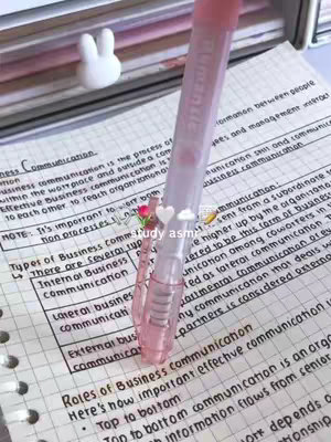 The image shows a close-up of a notebook with handwritten notes, a pink pen is partially in the frame with the pen in focus. There is a small bunny figure in the top left corner. The pen seems to be overlaying text that has been added to the cover image.