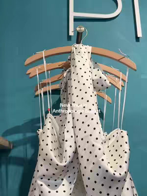 The image shows a fashion display with an off-white fabric with black polka dots draped over several wooden hangers. The hangers are arranged, and a teal-colored wall forms the backdrop. Text overlayed indicates a new find.