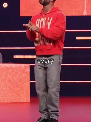 The image shows a man dressed in a red hooded sweatshirt and gray jeans on a stage with a dark background. The man is gesturing with his hands and the word 'every' is overlaid on the scene.