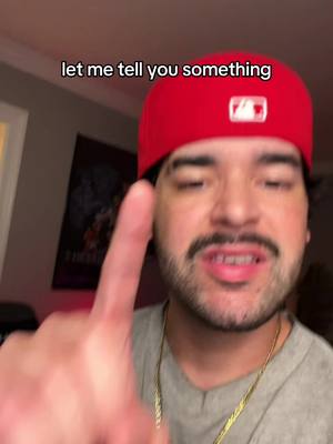The cover image is a selfie-style shot featuring a man in the center. He's wearing a red baseball cap with a white logo, a gray t-shirt, and a gold chain. He is pointing a finger towards the viewer and appears to be speaking. Behind him is a room with a poster on the wall. The overall composition is a head and shoulders shot with the man filling most of the frame.