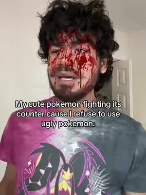 The cover image shows a young man from the chest up, with dark curly hair and a beard. His face is splattered with what appears to be fake blood, creating a dramatic and somewhat comical effect. He is wearing a tie-dye t-shirt with a two-tone design of purple and gray and black. Overlayed on the shirt is an image of a cartoon character. Just above the man’s head is an added text.
