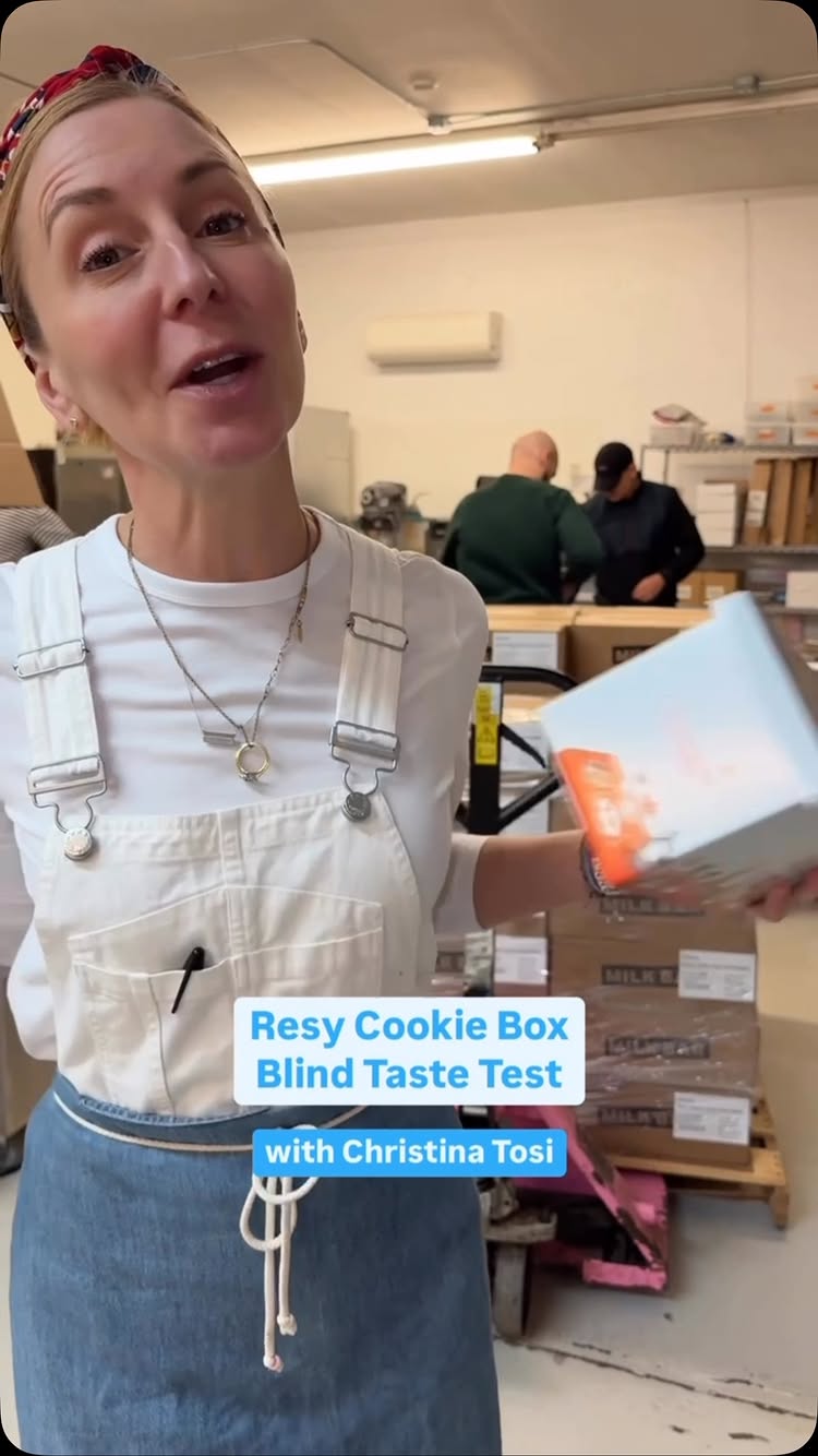 The image shows a woman standing in front of a pallet of boxes, holding a box with a cookie design. She is wearing a white shirt, overalls, and a bandana. Text overlay on the image says 'Resy Cookie Box Blind Taste Test with Christina Tosi'.