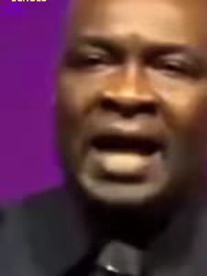 Close-up shot of a Black man, Apostle Joshua Selman, speaking to the camera with a background with purple gradient. The man has short, dark hair and is wearing a black suit. His facial expression suggests he is in mid-speech.