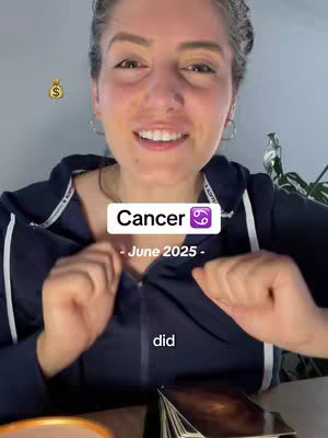 A woman with fair skin and light-colored hair smiles directly at the camera. She wears a navy blue zip-up hoodie over a white t-shirt. Text overlays include "Cancer" with the Cancer zodiac symbol, "-June 2025-", and the word "did". A golden money bag emoji is also present, alongside a deck of tarot cards.