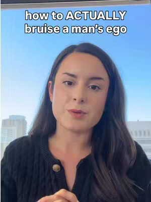 A medium shot of a woman with long, dark hair looking directly at the camera. She is wearing a black sweater, and the background shows a clear blue sky through what appears to be a window in a high-rise building.