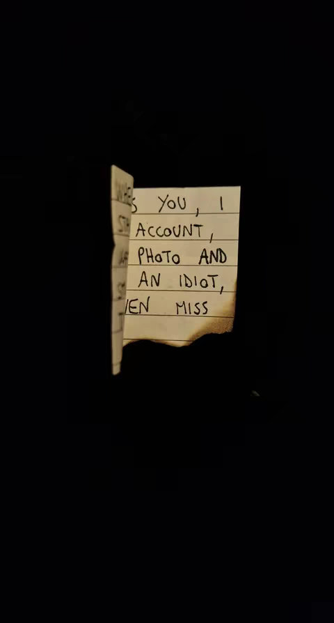 A photograph with a stark black background. The focus is on a torn piece of paper, slightly curled, with handwritten lines. The paper's edges are ragged, and there is evidence of scorching at the bottom. Phrases are visible in a handwritten font.